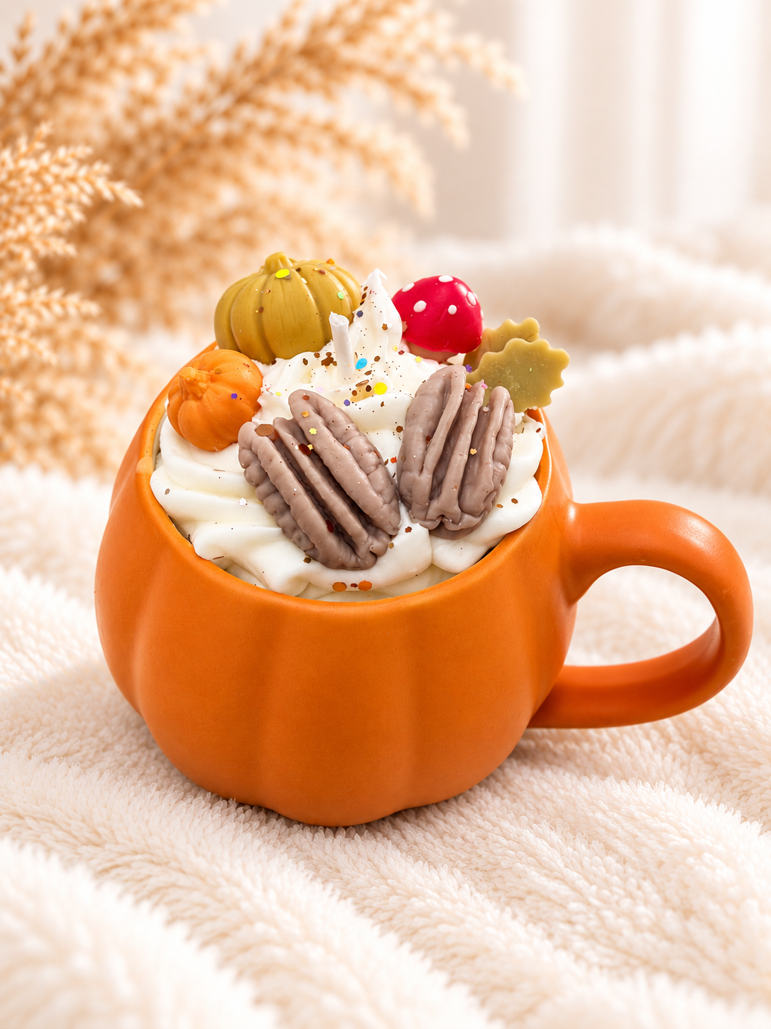 Orangefarbene Kürbis-Tassenkerze mit weißem Duftwachs und herbstlichen Wachselementen